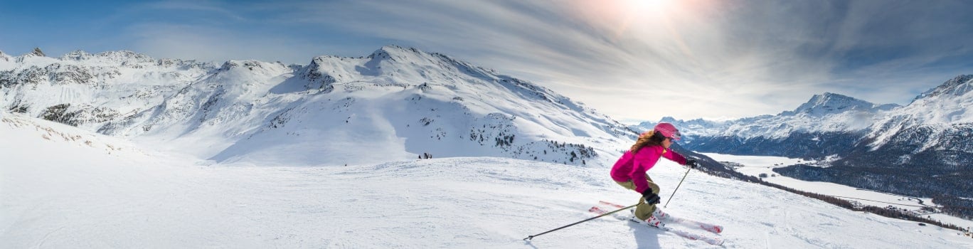 une femme vetue d'une combinaison de ski rose fait du ski sur la neige dans les montagnes