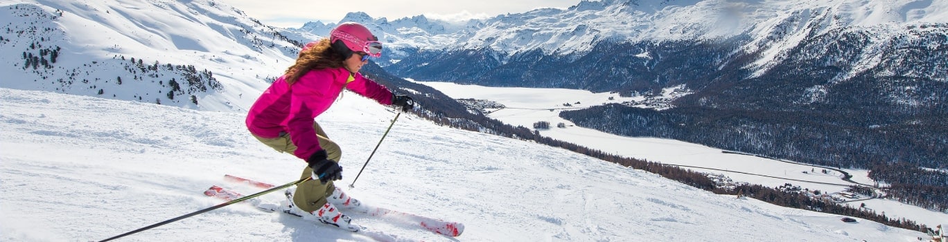 une femme vetue d'une combinaison de ski rose fait du ski sur la neige dans les montagnes